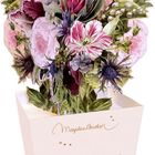 "Marjolein Bastin" steht auf einem cremefarbenen Behälter. Darin steckt eine bunt illustrierte Blumenkombination.