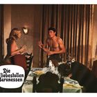 "Die liebestollen Baronessen." Eine dramatische Szene mit einem Mann ohne Hemd, einer Frau und einem am Tisch sitzenden Mann.