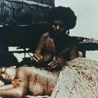 Kein Text vorhanden. Zwei Personen; eine liegt auf dem Bauch, die andere sitzt und macht möglicherweise Kunst auf dem Rücken.