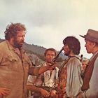 Eine Gruppe Männer in Westernkleidung, ein Mann hält einem anderen eine Pistole an den Kopf.