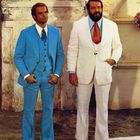 Zwei Männer vor einem antiken Gebäude. Der eine trägt einen blauen Anzug, der andere einen weißen Anzug.