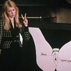 Text: "Clitoris", "Vaginal opening". Eine Frau zeigt auf ein Diagramm mit beschrifteten Teilen und macht ein Peace-Zeichen.