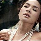 Ich kann die Personen nicht identifizieren. Eine Frau trägt Perlenketten, steht einem Mann nahe, der eine Mütze trägt.