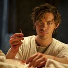 Ich erkenne keinen Text. Ein Mann in einem weißen Gewand hält einen blutigen Gegenstand und blickt konzentriert.