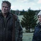 Zwei Personen, eine ältere und eine jüngere, stehen draußen in warmen, gepolsterten Kleidern vor einer bewaldeten Landschaft.