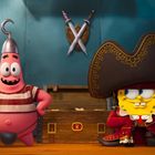 Zwei Figuren in Piratenkostümen stehen vor einer Schatztruhe. Links trägt eine Figur einen Hakenhelm, rechts trägt eine große Piratenmütze.