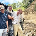 Drei Personen stehen lächelnd vor einem schmutzigen Geländewagen, im Hintergrund eine Erdrutsch-Szenerie.
