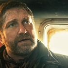 Ein Mann mit Bart, dreckigem Gesicht, in Lederjacke und Schal, sitzt in einem Fahrzeug mit hellem Fenster im Hintergrund.