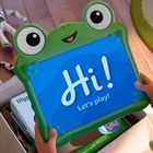 „Hi! Let's play!“ steht auf einem blauen Bildschirm in einem Frosch-Rahmen. Darum liegen Spielzeugfiguren auf dem Holzboden.