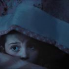 Ein Kind schaut mit großen Augen unter einer bunten Decke hervor, die mit Blumenmuster verziert ist.