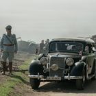 Nummernschild zeigt "IA-134431". Ein Mann in Uniform steht neben einem alten Auto mit NS-Symbolen im Freien.