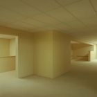 Ein leerer Raum mit hellgelben Wänden und Deckenplatten, ohne Fenster oder Dekorationen. Ein labyrinthartiges Layout.