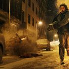 Ich kann den Text nicht erkennen. Eine Person rennt panisch eine verschneite Straße entlang, umgeben von Explosionen und geparkten Autos.