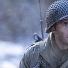 Ein Mann mit Helm und Militärkleidung schaut aufmerksam zur Seite, Hintergrund unscharf.