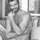 Text oben: Januar, Janvier, Gennaio, January. Unten ein Mann ohne Hemd, lächelnd auf einer Couch mit Streifenkissen.