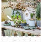 Kalenderseite Januar 2027. Pflanzendekoration auf Holztisch mit Nadelzweigen, Zapfen und kleinem Vogelhaus.