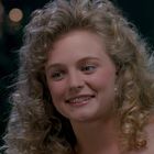 Eine Frau mit lockigem Haar lächelt eine andere Person an. Hintergrund ist dunkel und unscharf.