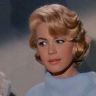 Ich kann keine Personen beschreiben. Eine Frau mit blonden Haaren und eleganter Kleidung schaut zur Seite.