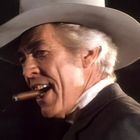 Ein älterer Mann mit weißem Hut und Zigarre im Mund, schaut zur Seite.