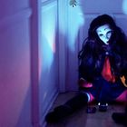 Eine Person in Schuluniform mit einer Maske sitzt auf dem Boden eines dunklen Flurs, umgeben von violettem Licht.