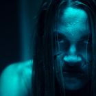 Eine junge Frau mit nassem Haar und ernstem Ausdruck, beleuchtet von blauem Licht.