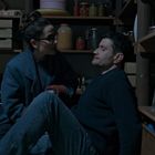 Ein Mann und eine Frau sitzen in einem dunklen Raum mit Regalen voller Vorratsgläser. Ein Kind schaut zu.