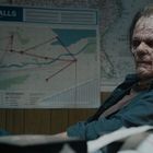 Oben steht "POWER FALLS". Eine Person mit vernarbtem Gesicht sitzt vor einer Karte mit eingezeichneten Linien.