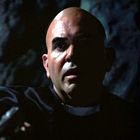 Ein Mann mit ernster Miene hält eine Waffe, neben ihm steht eine unheimlich geschminkte Nonne in Dunkelheit.