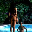 Zwei Personen am Pool. Eine Frau steht am Beckenrand, ein Mann im Wasser. Umgeben von Bäumen mit lila Lichtern.