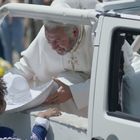 Ein lächelnder Mann in weißer Kleidung in einem Auto gibt einem Kind mit Sombrero die Hand.