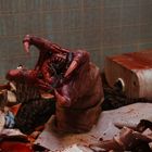Eine blutverschmierte Kreatur mit großen Zähnen erhebt sich aus einer zerstörten Umgebung, umgeben von Chaos und Zerstörung.