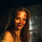 Es gibt keinen Text. Eine Person mit vernarbter Haut und dunklen Augen schaut in dämmriger Umgebung leicht lächelnd.