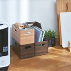 Holzkästen mit Zeitschriften und Pflanzen auf einem Holzboden. Eine Mikrowelle steht links. Schneidebretter im Hintergrund.