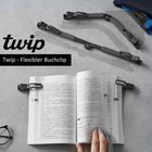 Twip - Flexibler Buchclip. Ein offenes Buch wird von Clips gehalten, darüber liegt ein faltbarer Buchclip.