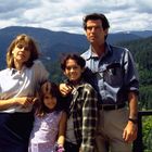Text auf einem Holzpfosten: "T63". Eine Familie steht vor einer Berglandschaft.