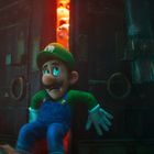 Ein ängstlicher Mann in grüner Kleidung lehnt an einer massiven Holztür mit orange leuchtendem Spalt dahinter.