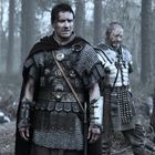 Zwei Männer in antiker Rüstung stehen erschöpft im Wald. Einer mit Kettenhemd und Umhang, der andere mit metallener Rüstung.