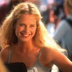 Ich kann den Namen oder den Inhalt des Textes nicht benennen. Eine Frau mit blonden Haaren lächelt in einer lebhaften Umgebung.