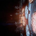 Eine futuristische Raumstation schwebt vor einem Planeten im Weltraum. Sechseckige Plattformen leuchten in Rotblau.