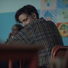 Ein junger Mann im karierten Hemd schaut über die Schulter. Im Hintergrund sind unscharfe Personen und bunte Wandbilder.