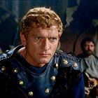 Ein Mann mit blondem Haar in römischer Rüstung, ernst blickend, im Vordergrund. Im Hintergrund eine weitere Person, unscharf.