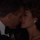 Ein Mann und eine Frau in eleganter Kleidung nähern sich für einen Kuss in einer dunklen Umgebung.