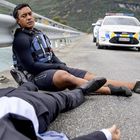 „Police” steht auf einem Auto im Hintergrund. Ein Mann in schwarzer Kleidung lehnt erschöpft am Geländer einer Straße.