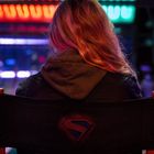 Eine Person sitzt auf einem Stuhl mit dem Superman-Logo, umgeben von bunten Lichtern in einer dunklen Umgebung.