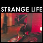 Text: "Strange Life". Eine Person sitzt auf einem Sofa in einem rot beleuchteten Raum mit Treppe im Hintergrund.