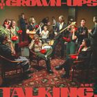 „The Grown-Ups Are Talking“ in roter Schrift. Viele Menschen sitzen oder stehen mit roten Telefonen in einem Raum.
