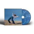 Eine Person tanzt in weiter Jeans in einer Wüstenlandschaft. Daneben ist eine CD-Hülle mit blauen Mustern.