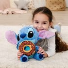 Ein Kind liegt auf einem Teppich und umarmt ein blaues Stofftier mit großen Ohren und Donut in den Händen.