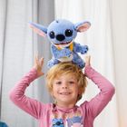Ein Kind trägt ein rosa Shirt mit "Stitch"-Motiv und hält ein großes blaues Plüschtier desselben Charakters über dem Kopf.