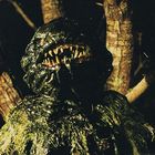 Keine erkennbaren Texte. Eine Kreatur mit schlammigen Zähnen und dunklem, schleimigem Körper vor einem Baum.